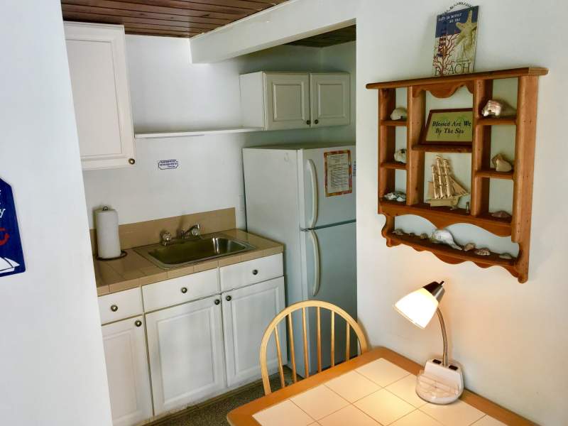 White kitchen cabinets, sink, refrigerator. Partial view of two person table